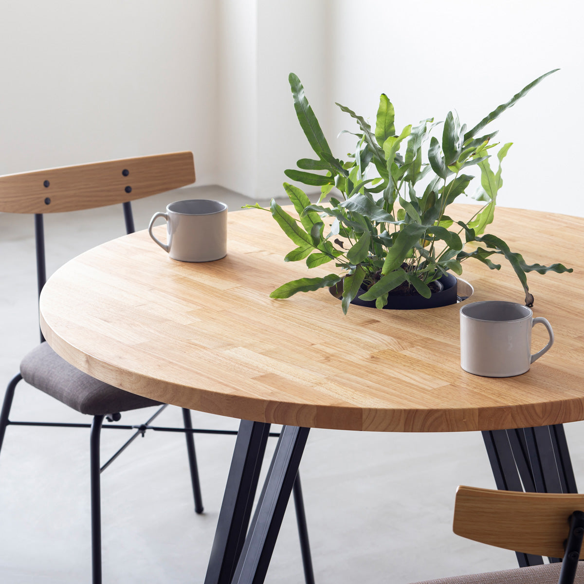 KANADEMONOのワイヤーバスケット付きのラバーウッド材ナチュラルのラウンド天板にマットブラックのトライアングル鉄脚を組み合わせたカフェテーブル（使用例2）