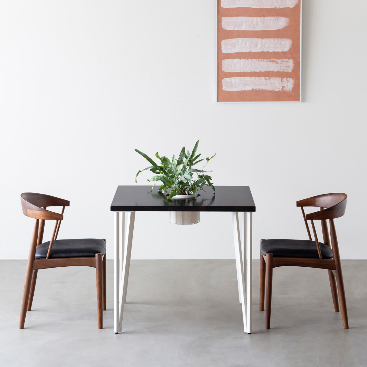 KANADEMONOのワイヤーバスケット付きのラバーウッド材ブラックブラウンのスクエア天板にマットホワイトのトライアングルStraight鉄脚を組み合わせたカフェテーブル（使用例）