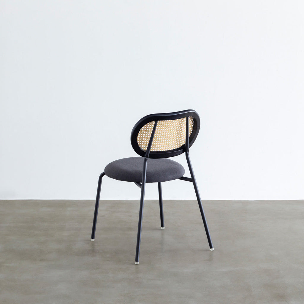 KANADEMONOのラタン調の楕円形の背もたれ、ダークグレーのファブリック座面、ブラックスチール脚が特徴のモダンなダイニングチェア（背面）