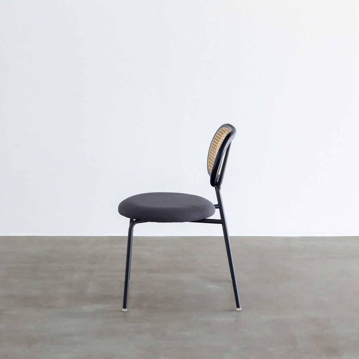 KANADEMONOのラタン調の楕円形の背もたれ、ダークグレーのファブリック座面、ブラックスチール脚が特徴のモダンなダイニングチェア（側面）