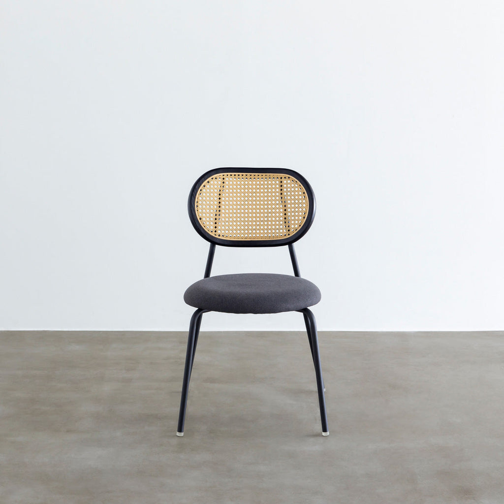 KANADEMONOのラタン調の楕円形の背もたれ、ダークグレーのファブリック座面、ブラックスチール脚が特徴のモダンなダイニングチェア（使用例3）