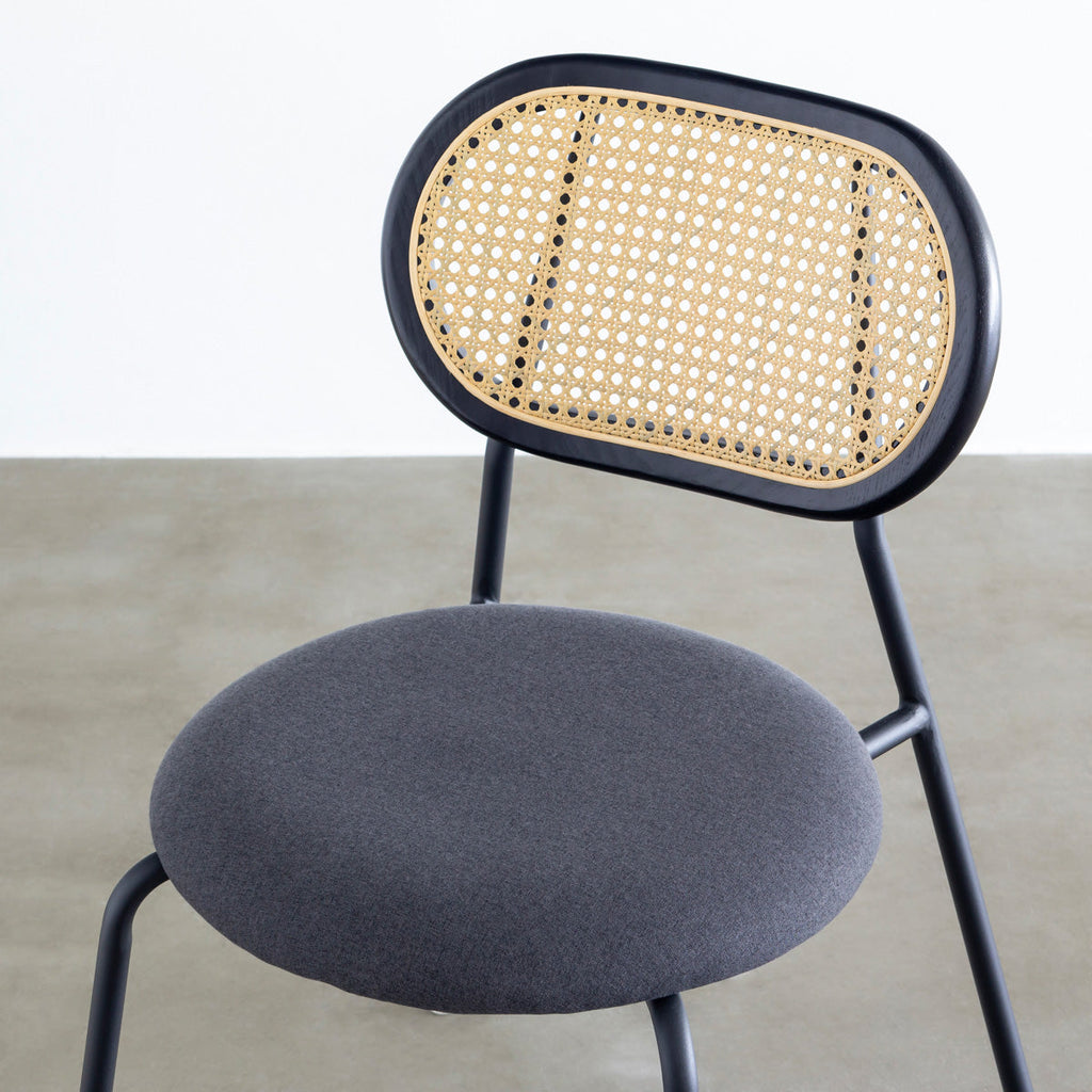 KANADEMONOのラタン調の楕円形の背もたれ、ダークグレーのファブリック座面、ブラックスチール脚が特徴のモダンなダイニングチェア（クローズアップ）