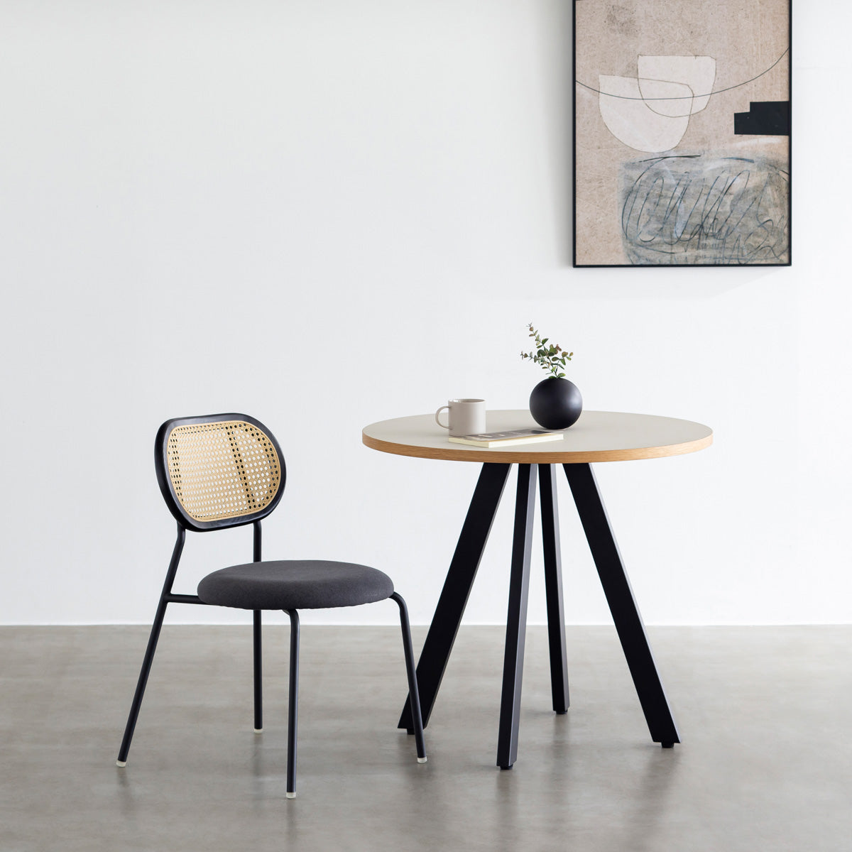 KANADEMONOのラタン調の楕円形の背もたれ、ダークグレーのファブリック座面、ブラックスチール脚が特徴のモダンなダイニングチェア（使用例）