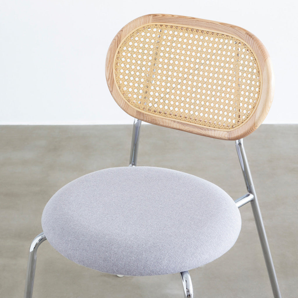 KANADEMONOのラタン調の楕円形の背もたれ、ライトグレーのファブリック座面、シルバースチール脚が特徴のモダンなダイニングチェア（クローズアップ）