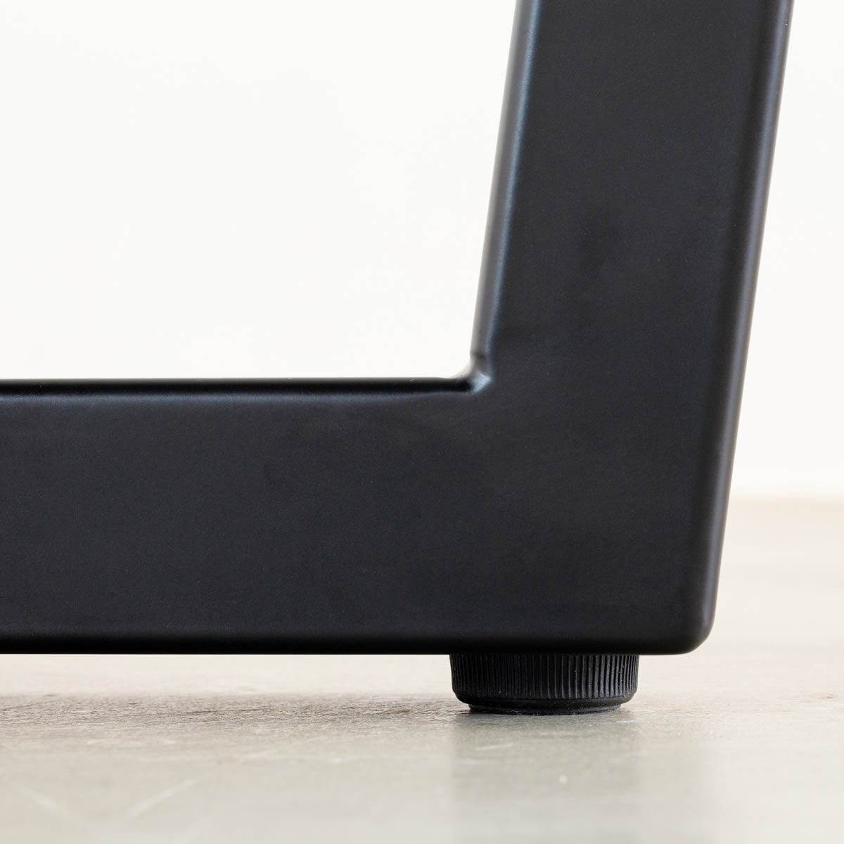 KANADEMONOのホワイトオーク突板天板とマットブラックのトラペゾイド鉄脚を組み合わせたシンプルモダンなテーブル（アジャスター部分）