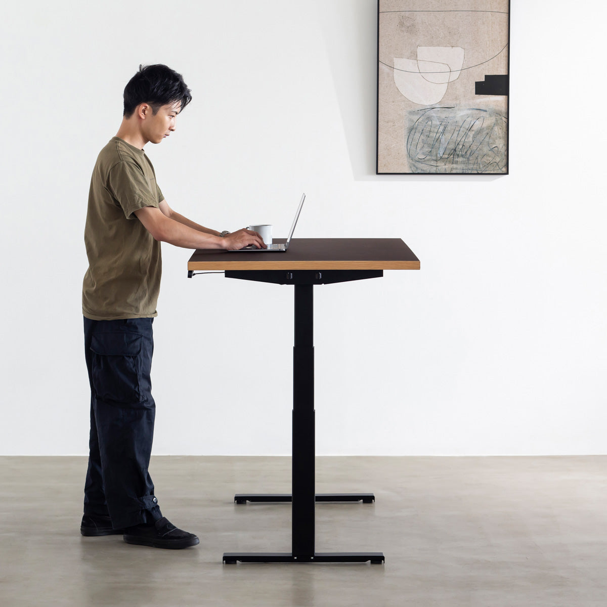 ファニチャーリノリウム素材のMauve天板と、ブラックの電動昇降脚を組み合わせた、デザイン性も機能性もスマートなテーブル（男性使用例）