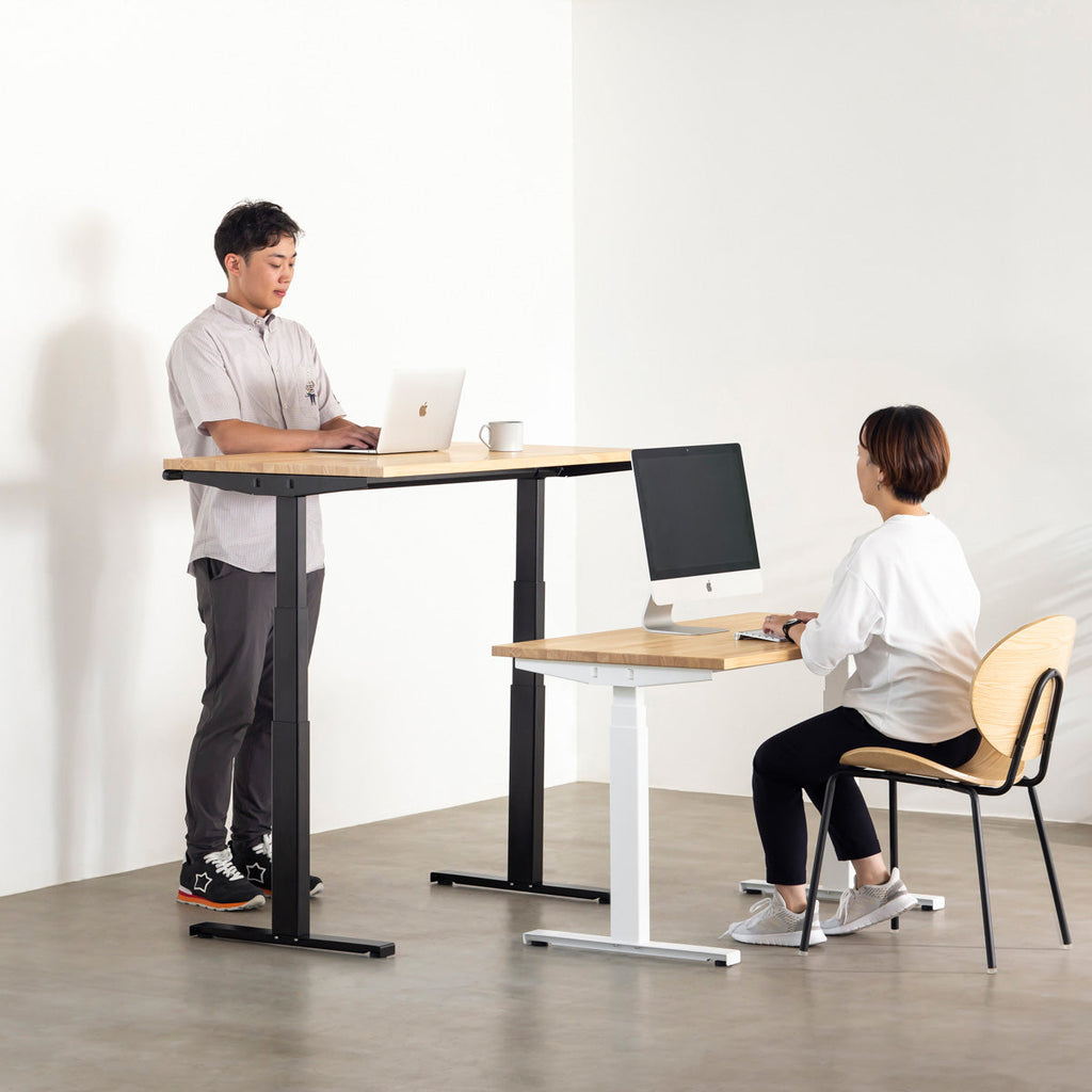 あたたかみ溢れるラバーウッドナチュラルの天板と、ブラックの電動昇降脚を組み合わせた、デザイン性も機能性もスマートなテーブル（組み合わせ使用例人入り）