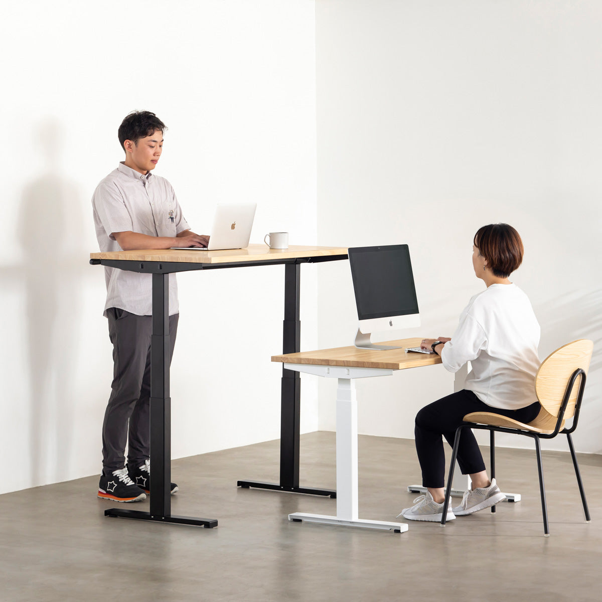 あたたかみ溢れるラバーウッドナチュラルの天板と、ブラックの電動昇降脚を組み合わせた、デザイン性も機能性もスマートなテーブル（組み合わせ使用例人入り）