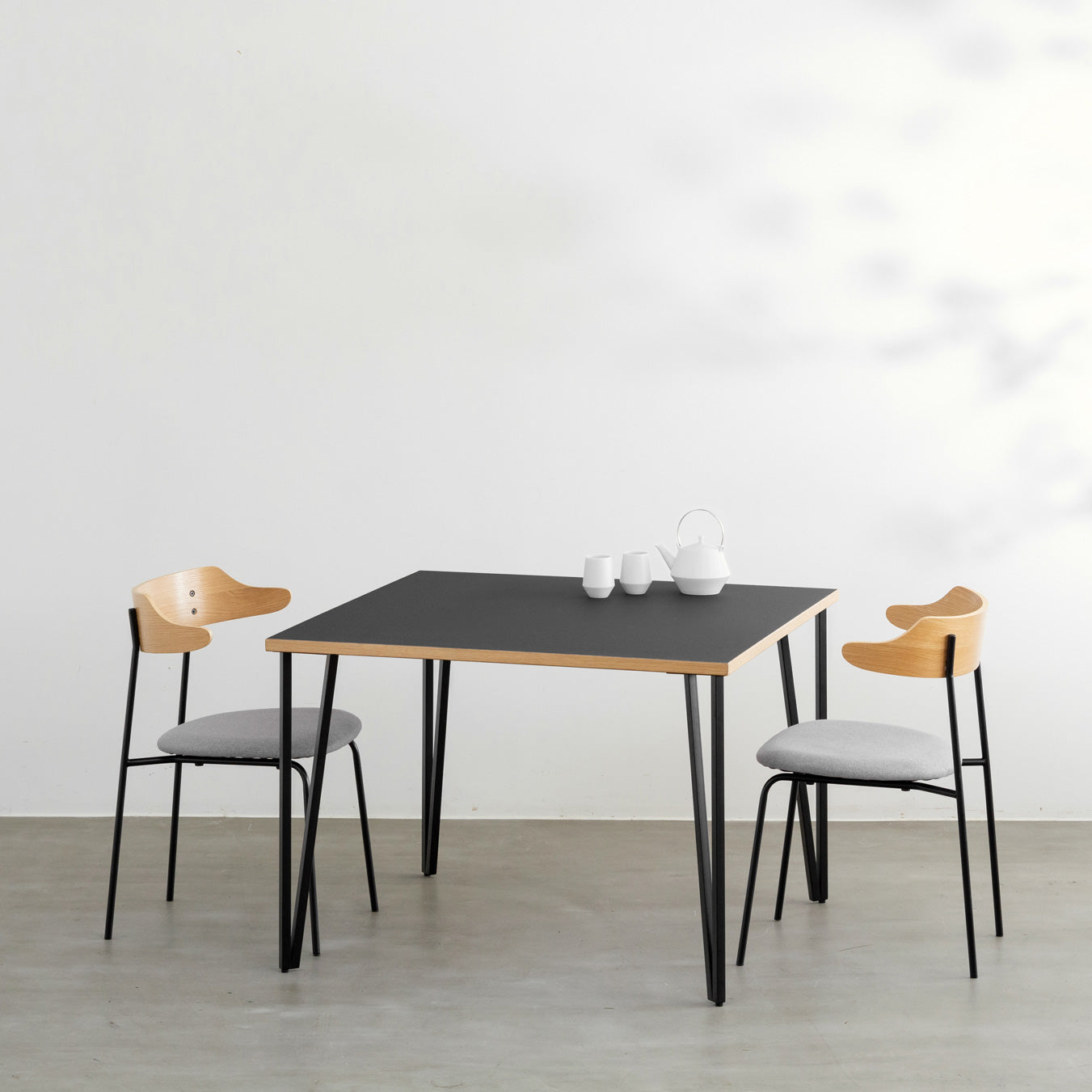 KANADEMONOのリノリウムNero天板とブラックトライアングルピン4本を組み合わせた一辺100cmスクエア型のカフェテーブル（使用例）