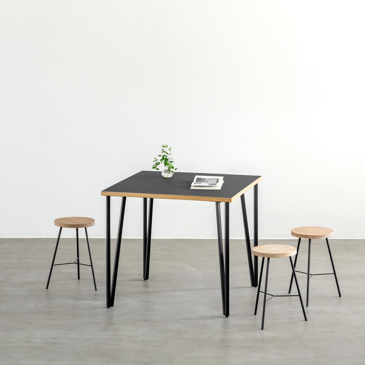 KANADEMONOのリノリウムNero天板とブラックトライアングルピン4本を組み合わせた一辺80cmスクエア型のカフェテーブル（使用例）